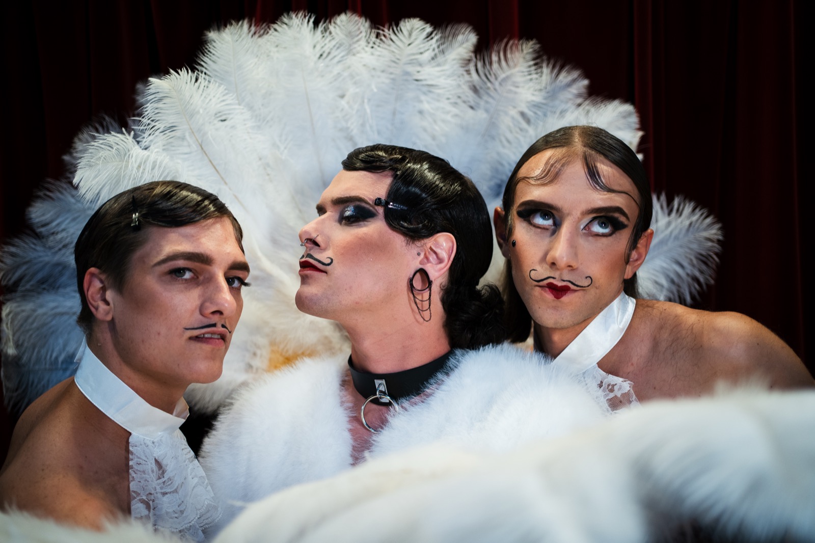 Three cabaret characters framed by white feathers