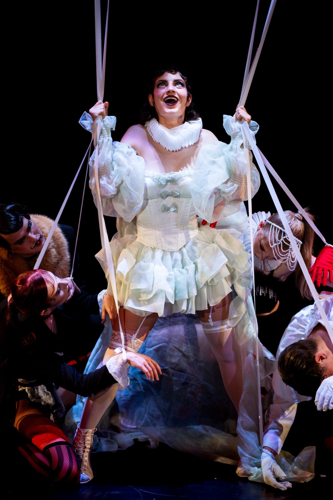 Character surrounded by ensemble and white ribbon costume elements